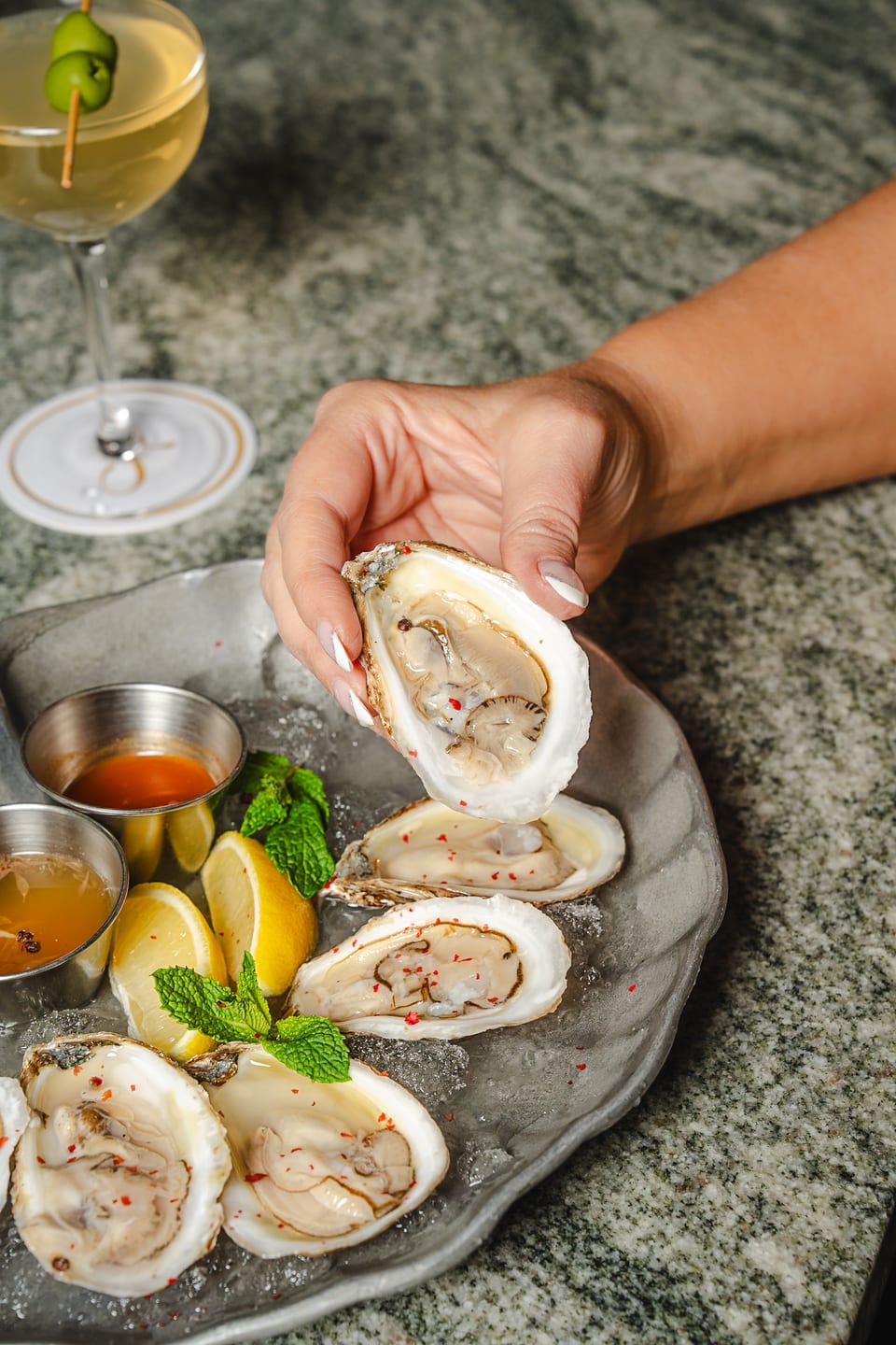 Hand holding a fresh oyster on the half shell with martini