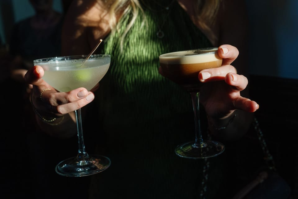 Two cocktails held by guests — lime martini and espresso martini in dramatic light