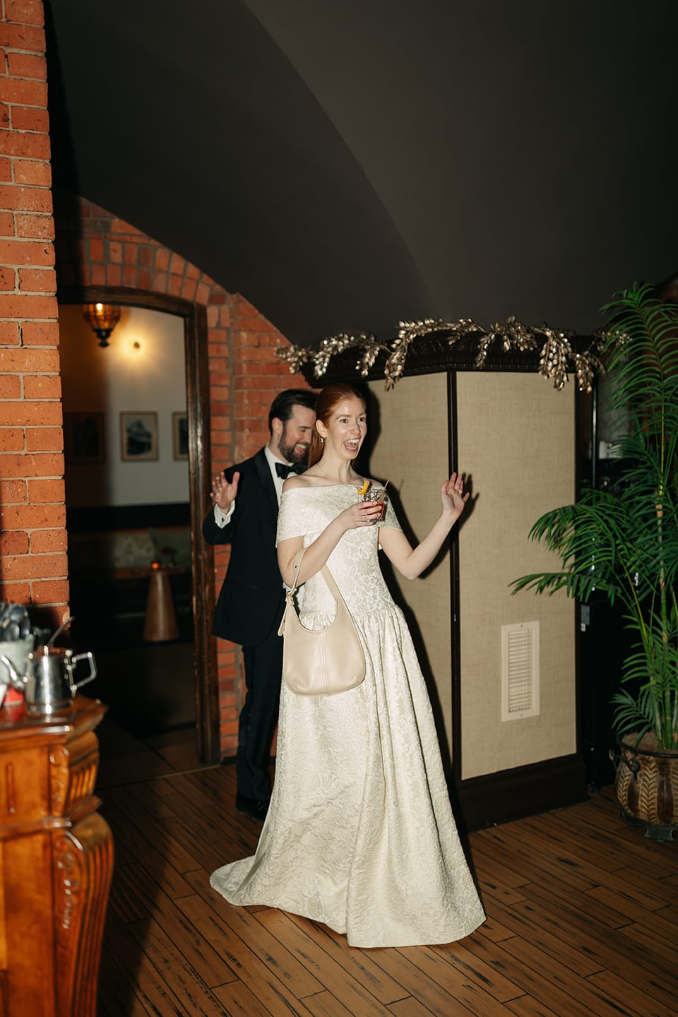Bride laughing during cocktail hour holding a drink, festive ribbon arch overhead