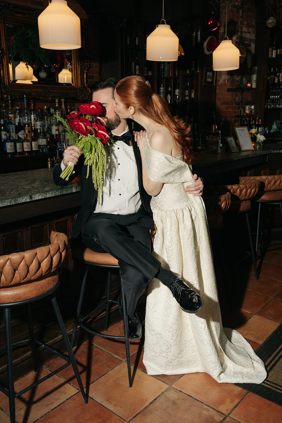 Bride and groom kissing at the bar with red anthurium bouquet